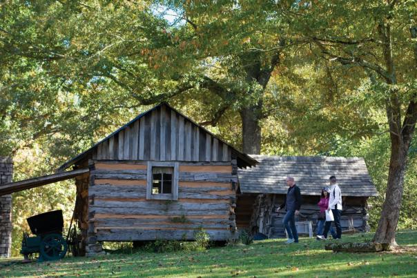 people walking by a historic log cabin