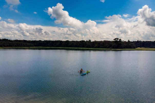 A drone shot of 3 colorful kayaks in a lake with a blue sky.