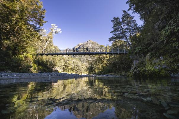 Ground of friends crossing a swing bridge on the Routeburn Track with a mountain in the background