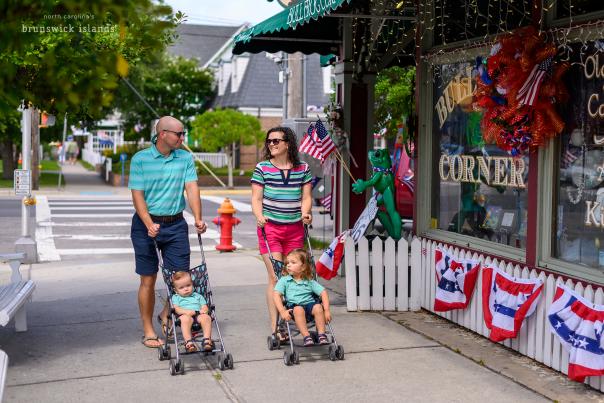 a mother and father pushing their two young kids in strollers through downtown Southport