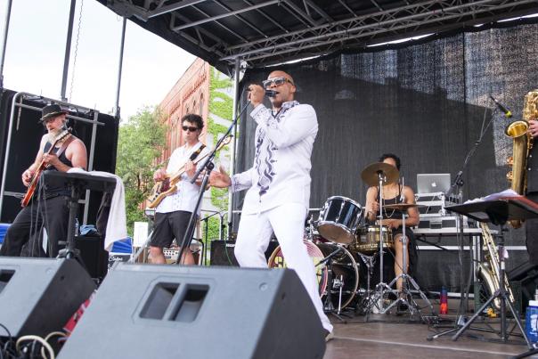 band of five musicians perform on an outdoor stage.