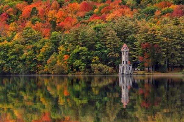 Kingfisher tower surrounded by colorful trees behind and reflected in a still lake in front.