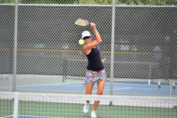 A white woman hits a pickleball with a racquet while playing on the court.