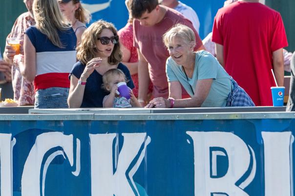 Two adult, white women and a toddler watch a Madison Night Mares softball game