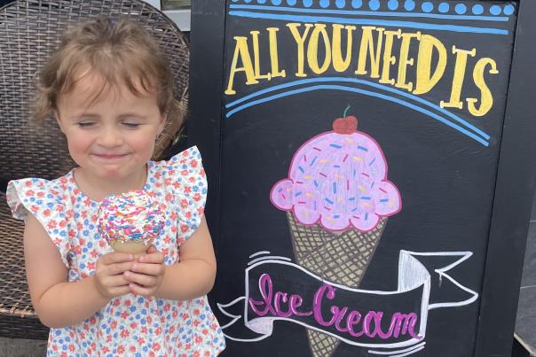 A child enjoys a cone of ice cream with sprinkles in front of Sweet Ride Ice Cream