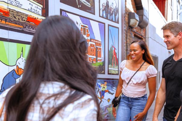 Four people smile and discuss a mural they are looking at.