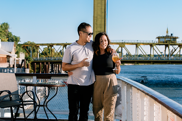 A smiling couple enjoying beverages and riverfront views