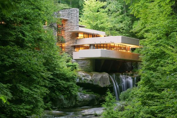 A modern home sitting on top of a waterfall with green trees surrounding it