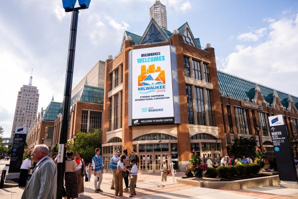 Attendees gather outside Baird Center in downtown Milwaukee beneath a large digital welcome sign for the 2026 Eternal Happiness International Convention.