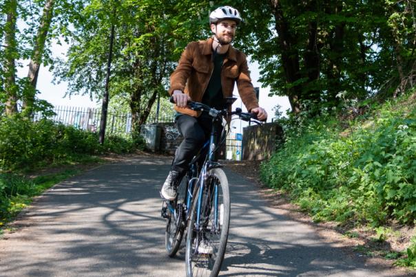 A man on a bike cycling down a path on a gentle hillside with greenery either side