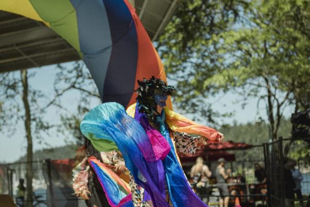 A person dancing in front of a rainbow dress in a flowy rainbow dress.