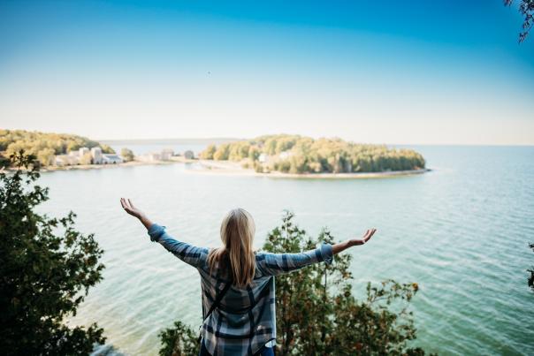 A woman with outstretched arms overlooking Lake Michigan at Fayette Historic State Park, located in the Upper Peninsula