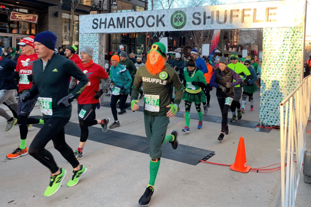 A man wearing a fake red beard and leprechaun hat crosses the finish like at the Shamrock Shuffle run