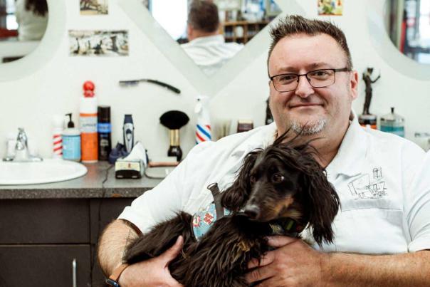 A man holds his dog at a barber salon.