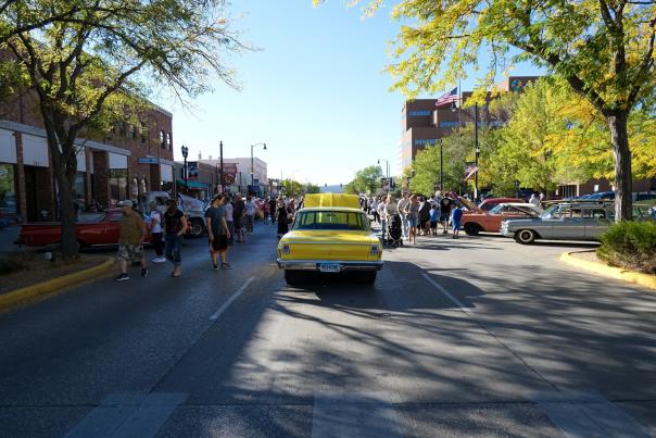 yellow classic car in the center of the street with people touring around them in downtown rapid city, sd