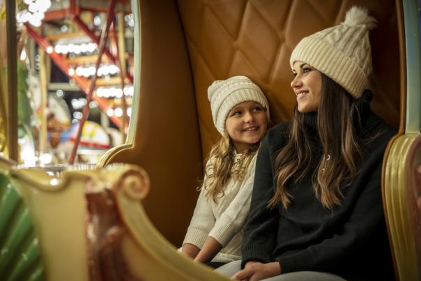 Woman and young girl sitting on bench on carousel in winterwear