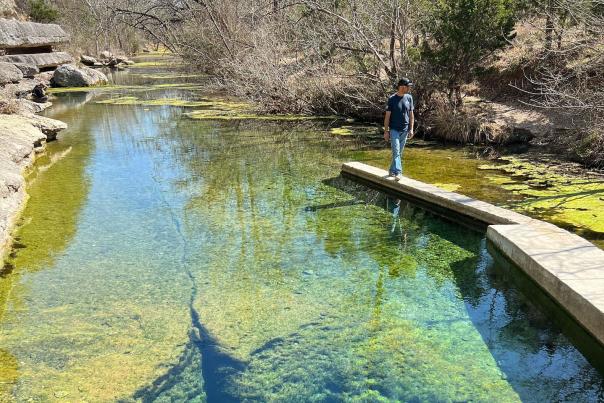 A woman sitting on the rock edge of Jacob's Well looking into the water.