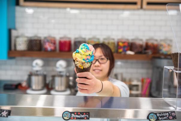woman holding colorful ice cream cone behind ice cream shop counter