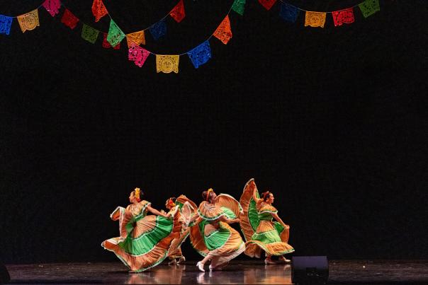 A group of five Hispanic women dance on stage at the Overture Center in colorful, cultural dresses