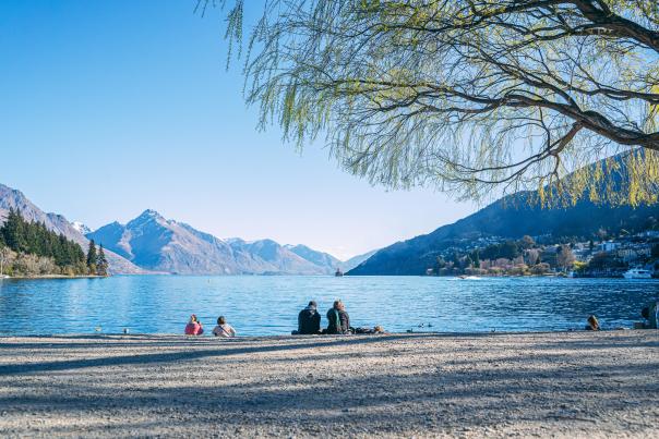 People sitting on Queenstown beach in spring with lake views and mountains in the background
