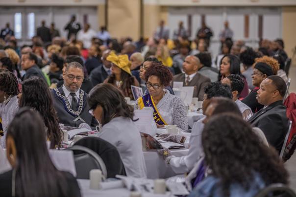 Large group of people seated at round tables attending a formal community banquet or conference indoors