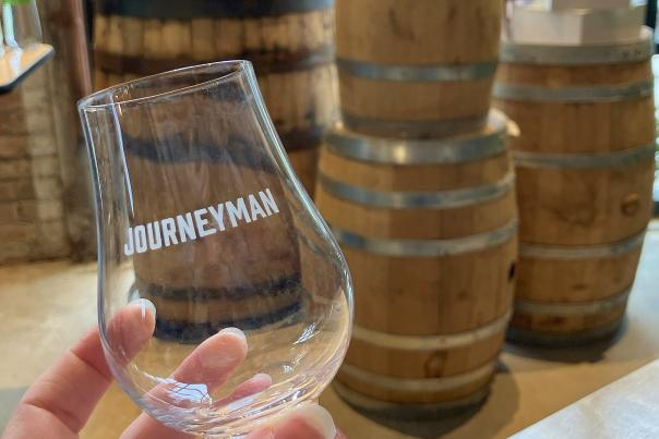 A hand holds a glass in front of barrels.