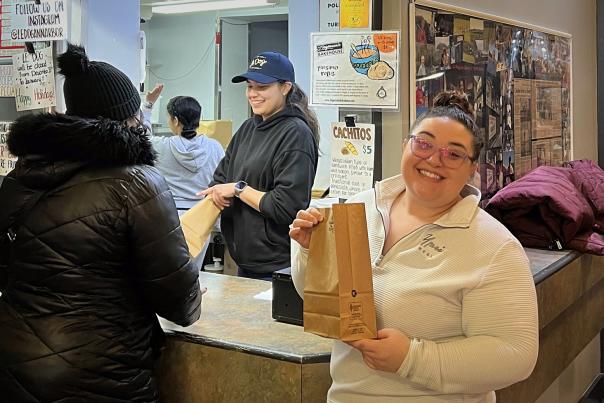 Woman poses holding lunch paper back after ordering to-go from a counter-service restaurant.
