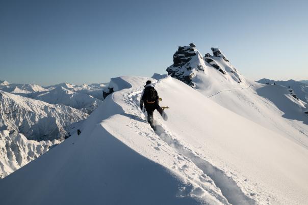 Snowboarder hiking to Treble Cone summit in powder