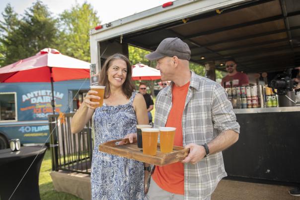 A man carrying a tray of beers and a woman walking with him with a beer in her hand at a festival
