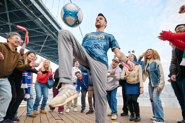 A man playing with a soccer ball with people cheering and standing around him