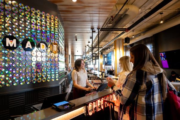 Two hotel guests check in with smiling front desk worker at The Moxy