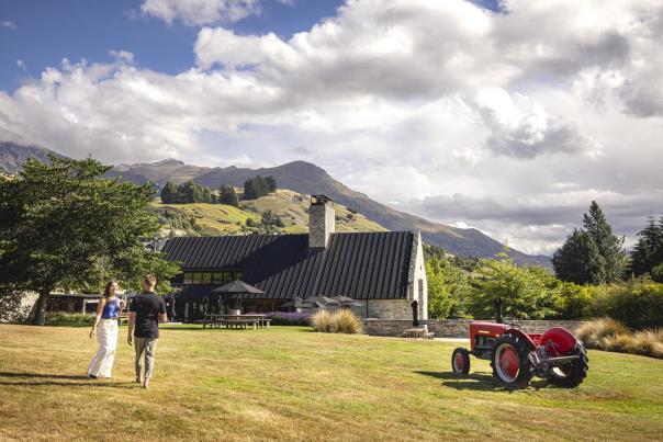 Two people walking along a lawn towards a restaurant with views of mountains in the background