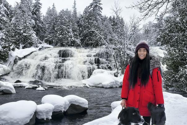 woman standing with 2 dogs in front of snowy Bond Falls, in the Upper Peninsula, Michigan