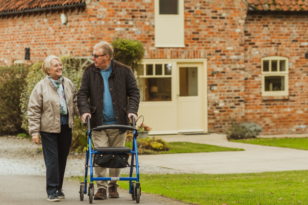 A couple walking the grounds at Broadgate Farm Cottages in East Yorkshire. The man is walking with the aid of a rollator.