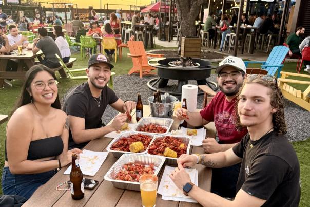 People sitting on a large outdoor patio at sunset enjoying crawfish on paper trays.