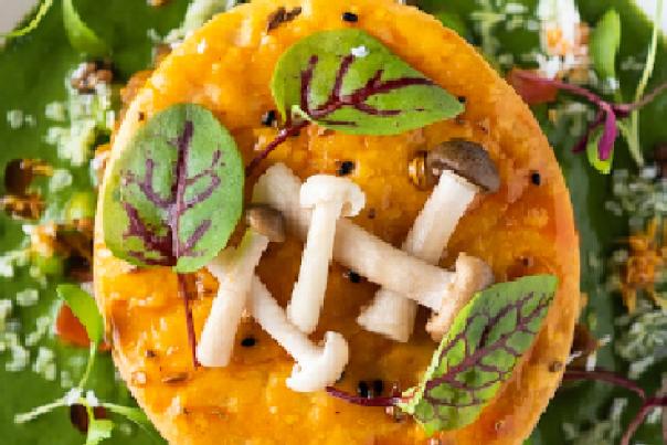 A white plate with a vibrant mushroom dish on a green sauce