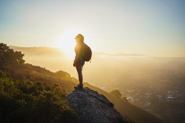 Hiker on rock looking up with the sunrise in the background