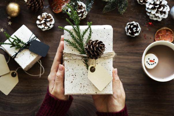 Photo of someone holding a wrapped gift with pinecones and hot chocolate on the table