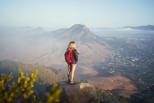 Solo hiker with red backpack looking out from mountain top