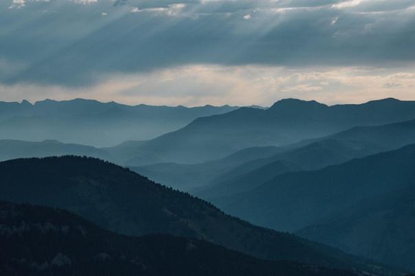 Layered mountain ranges under a cloudy sky, with soft light filtering through, creating a serene and expansive landscape.