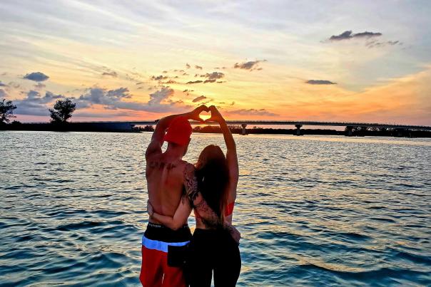 Couple standing in water at sunset, creating "heart hands"