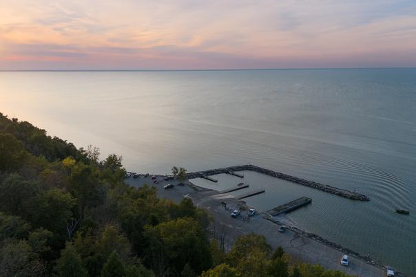 A drone shot of Bayshore County park, overlooking the water with trees in the foreground during sunset.