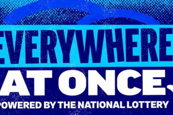 Everywhere at once logo. The background is blue with white writing. Underneath 'powered by the national lottery' is in white text.