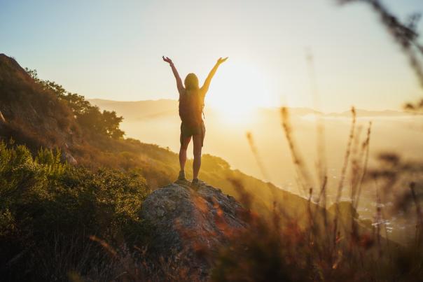 Hiker on a rock enjoying sunrise with hands up