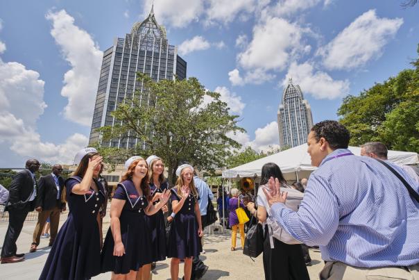 Young ladies in matching blue dresses welcome Amtrak train passengers with skyscrapers in the background