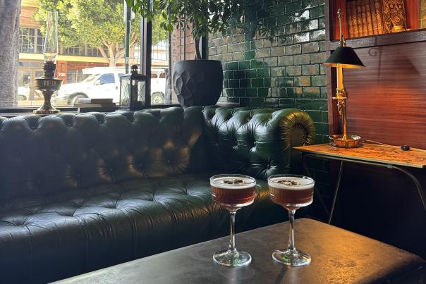 Two coop glass cocktails on a table in front of a green couch and library with a window to the street at Feral in downtown San Luis Obispo.