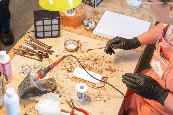 Woman in progress of a workshop demonstration. She's wearing black gloves and holding a crafting utensil in her right hand.