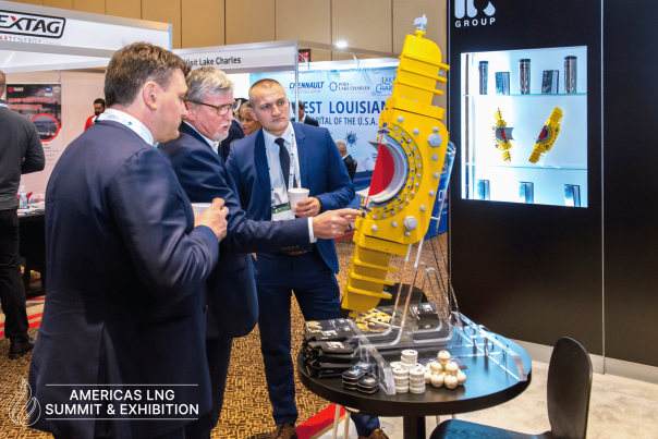 Three men in business attire examine a yellow industrial component at a booth during the Americas LNG Summit & Exhibition, with Visit Lake Charles and other local partners represented in the background.