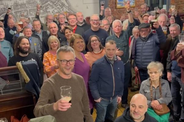 Shareholders inside the New Clarence pub raise their drinks glasses and smile