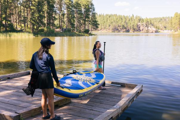 family carrying a paddle board down the dock to the waters edge in the black hills of south dakota